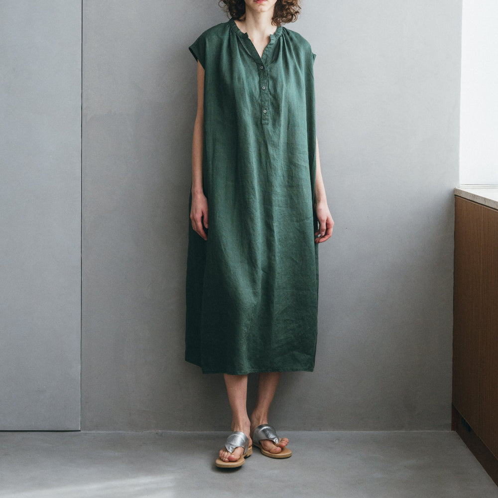 Woman wearing a green dress standing against a gray wall.