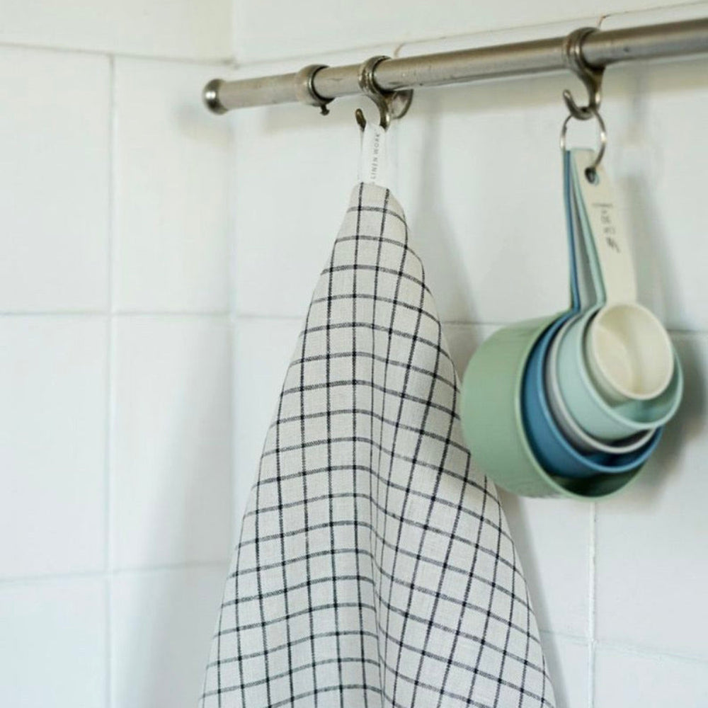 Grid-patterned towel and measuring cups hanging on a metal rod against a tiled wall.