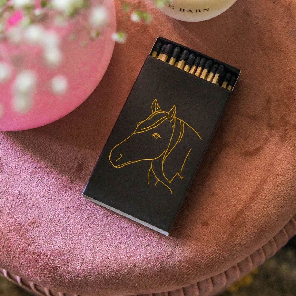 Matches with horse design on a pink surface next to a candle and flowers
