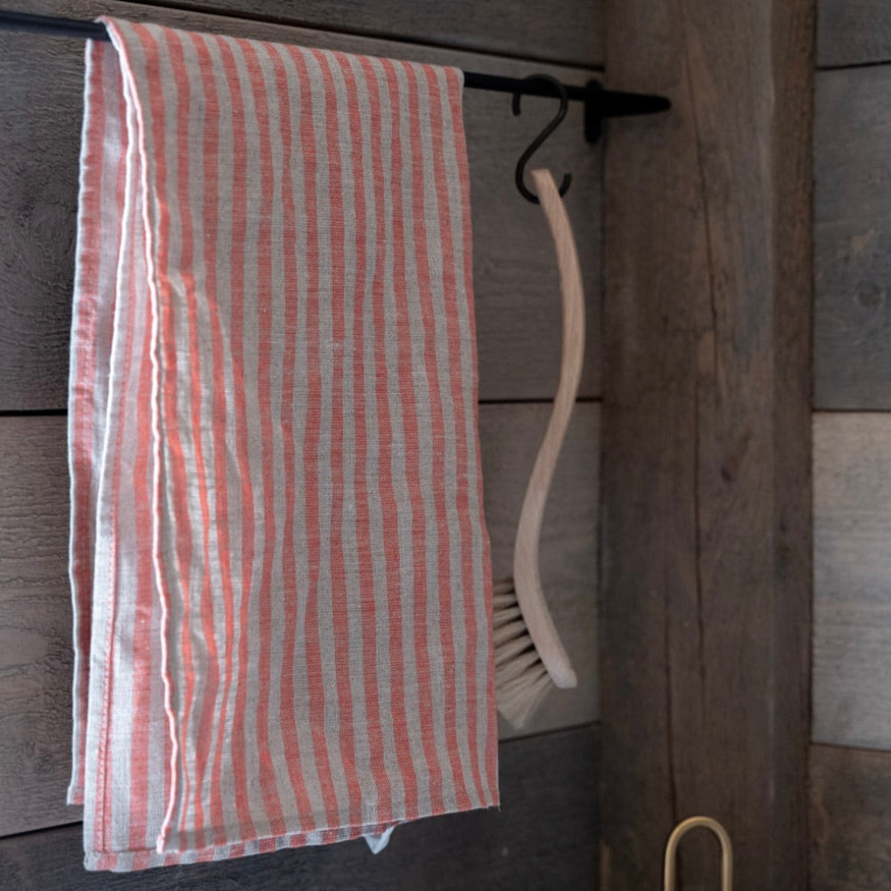 Striped towel hanging on a wooden wall with a brush and container below.