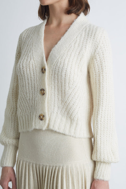 Person wearing a cream-colored knitted cardigan and skirt set on a white background