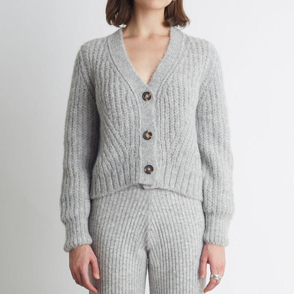 Woman wearing a gray ribbed cardigan and pants on a light gray background