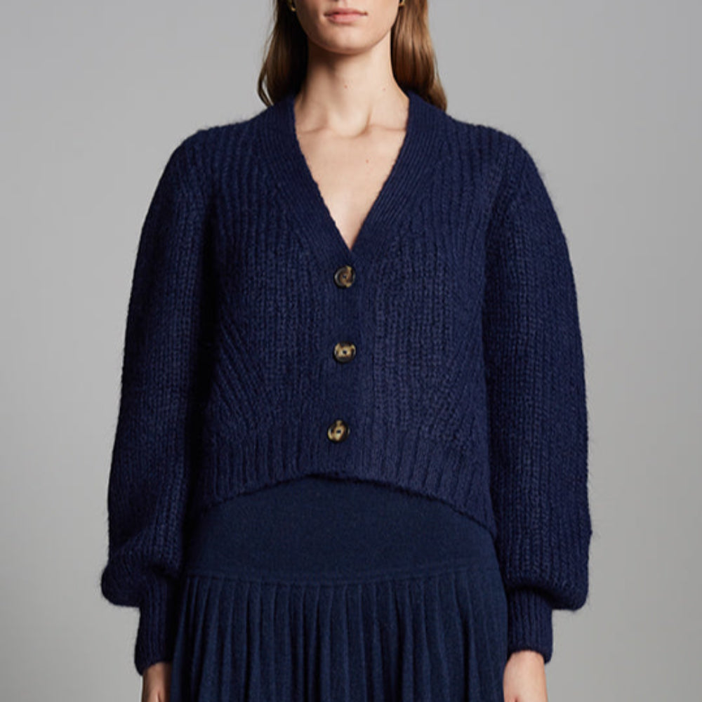 Woman wearing a navy blue knitted cardigan and skirt on a gray background