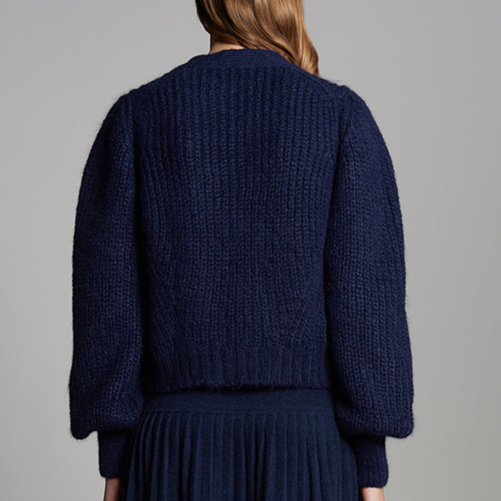 Person wearing a dark blue knitted sweater and skirt set against a gray background