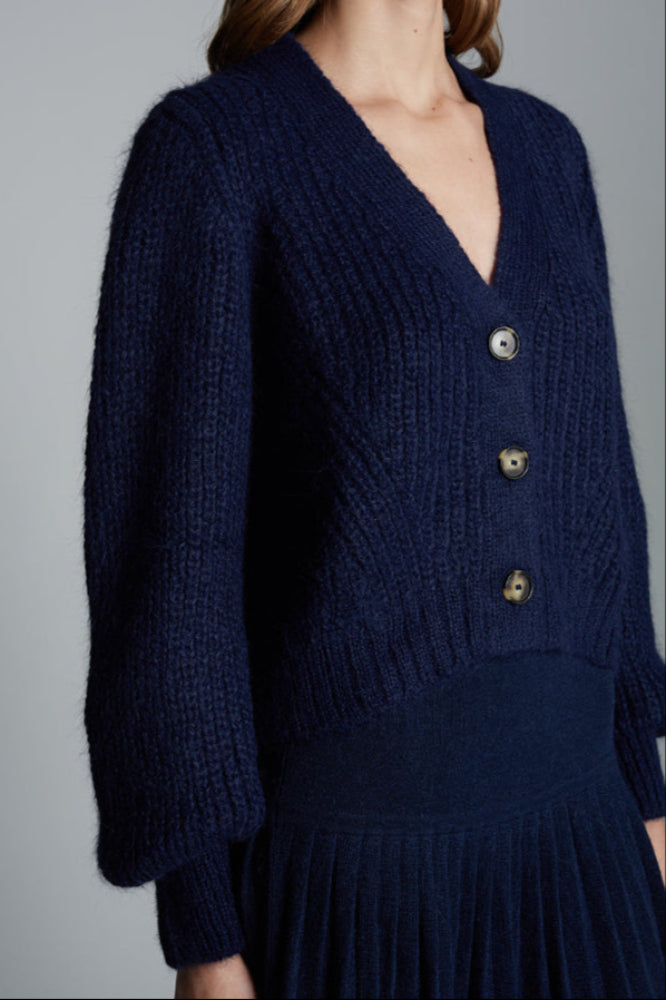 Navy blue knitted cardigan worn by a person on a gray background