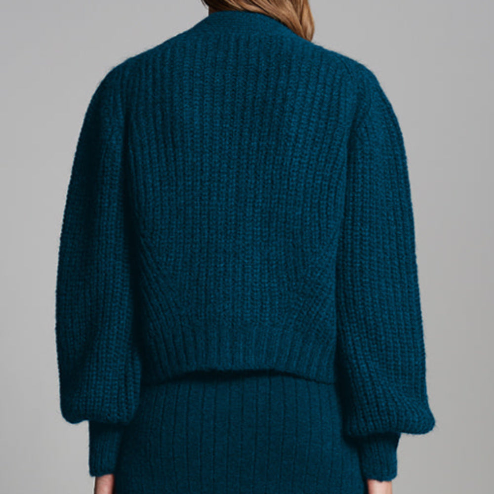 Person wearing a teal sweater and skirt set against a gray background