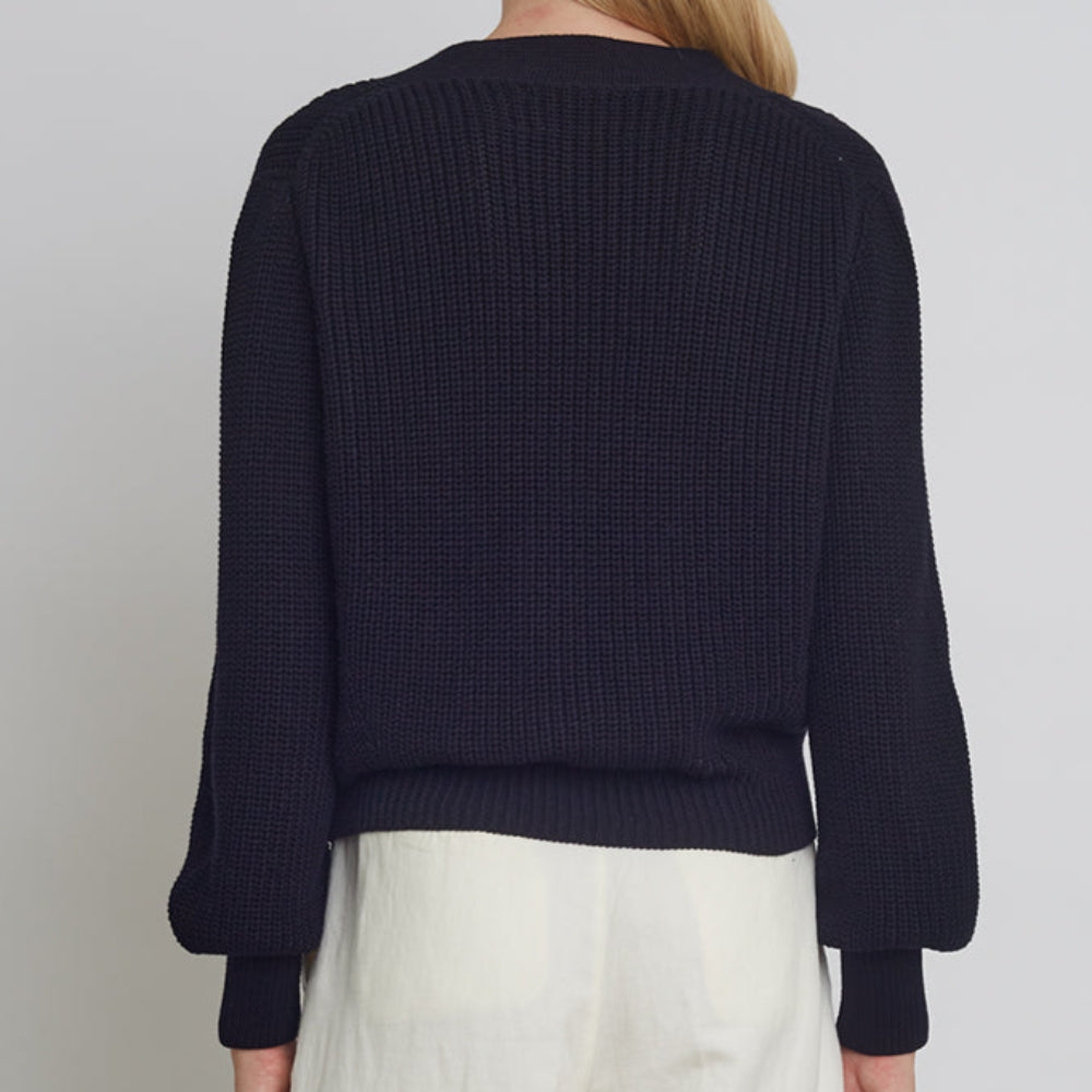 Person wearing a navy sweater and white pants on a plain background