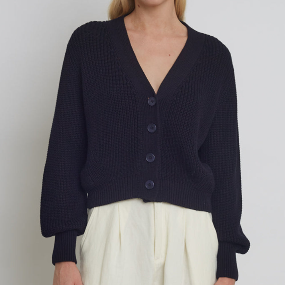 Woman wearing a navy blue cardigan and white pants against a plain background