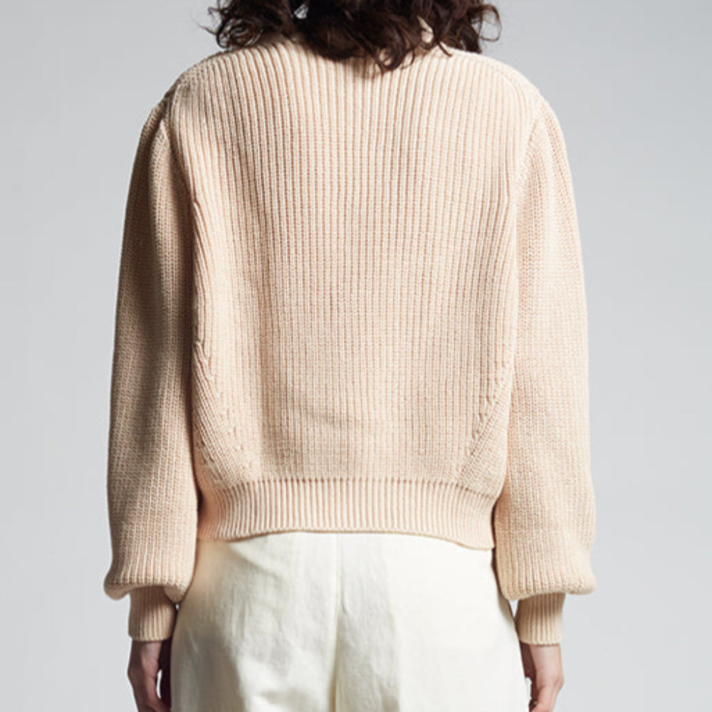 Person wearing a beige sweater and white pants on a plain background