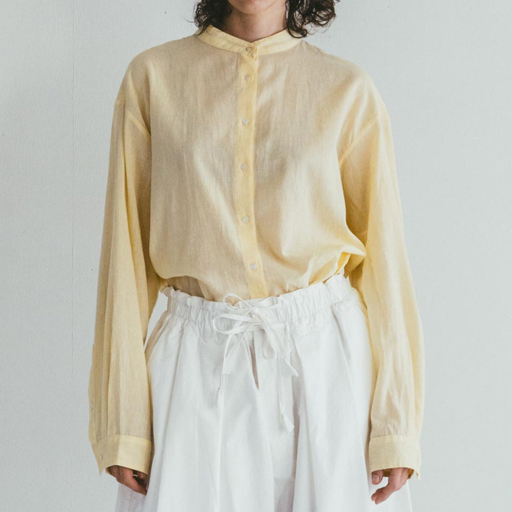 Person wearing a light yellow shirt and white pants against a plain background