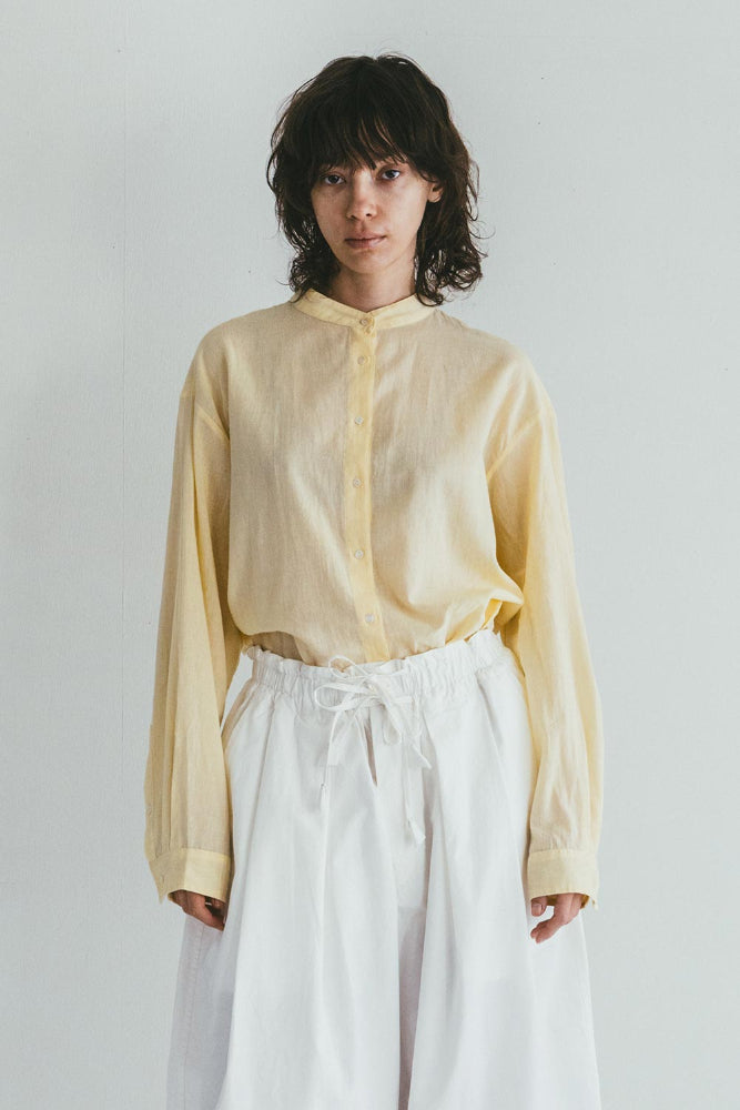 Person wearing a light yellow shirt and white pants against a plain background