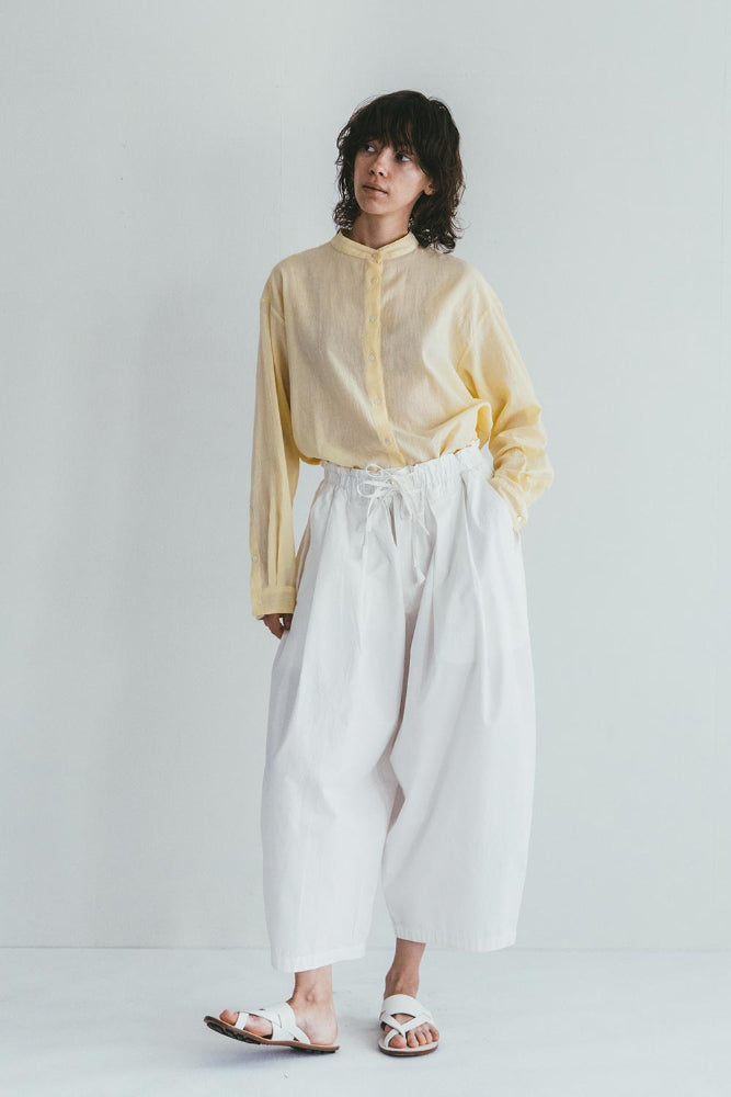 Person wearing a yellow shirt and white pants on a plain background