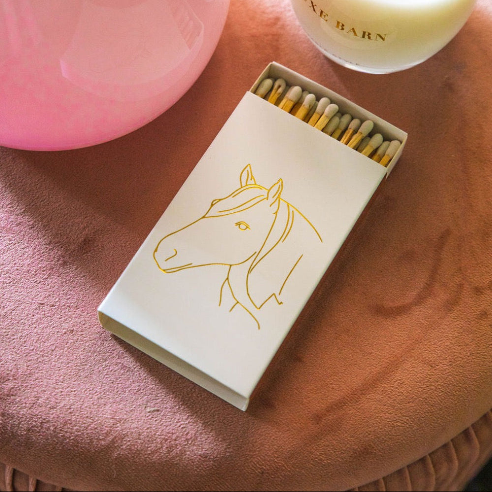 Matchbox with horse illustration next to a candle on a pink surface