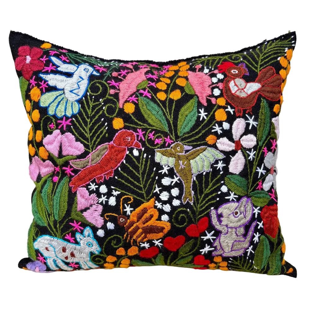 A square black embroidered throw pillow featuring a vibrant, multicolored nature and bird pattern with birds, flowers, butterflies, and a frog