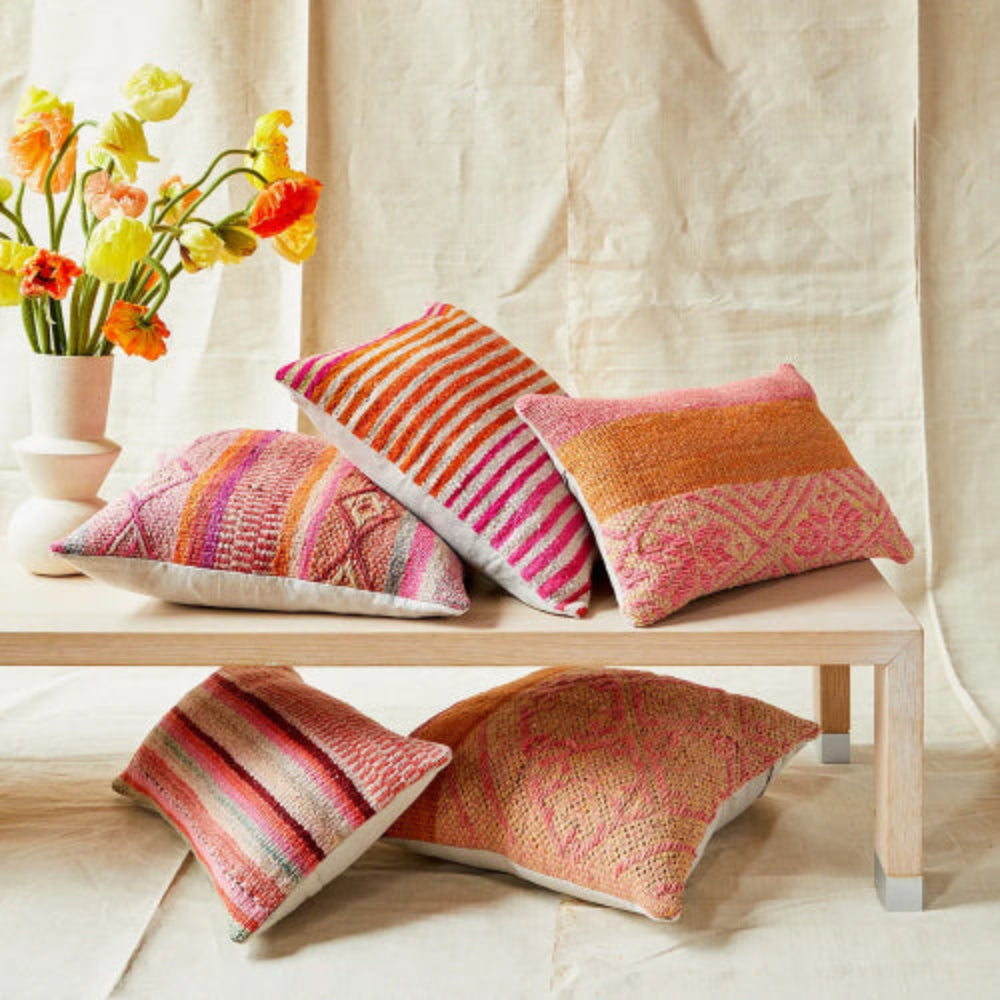 Colorful patterned pillows on a wooden bench with flowers in the background