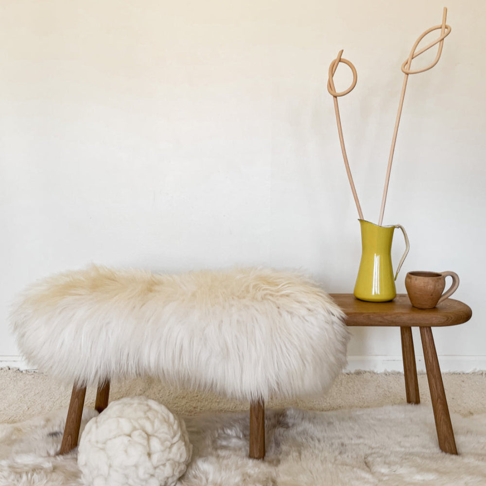 wooden bench with a vase and cup, next to a white sheepskin throw