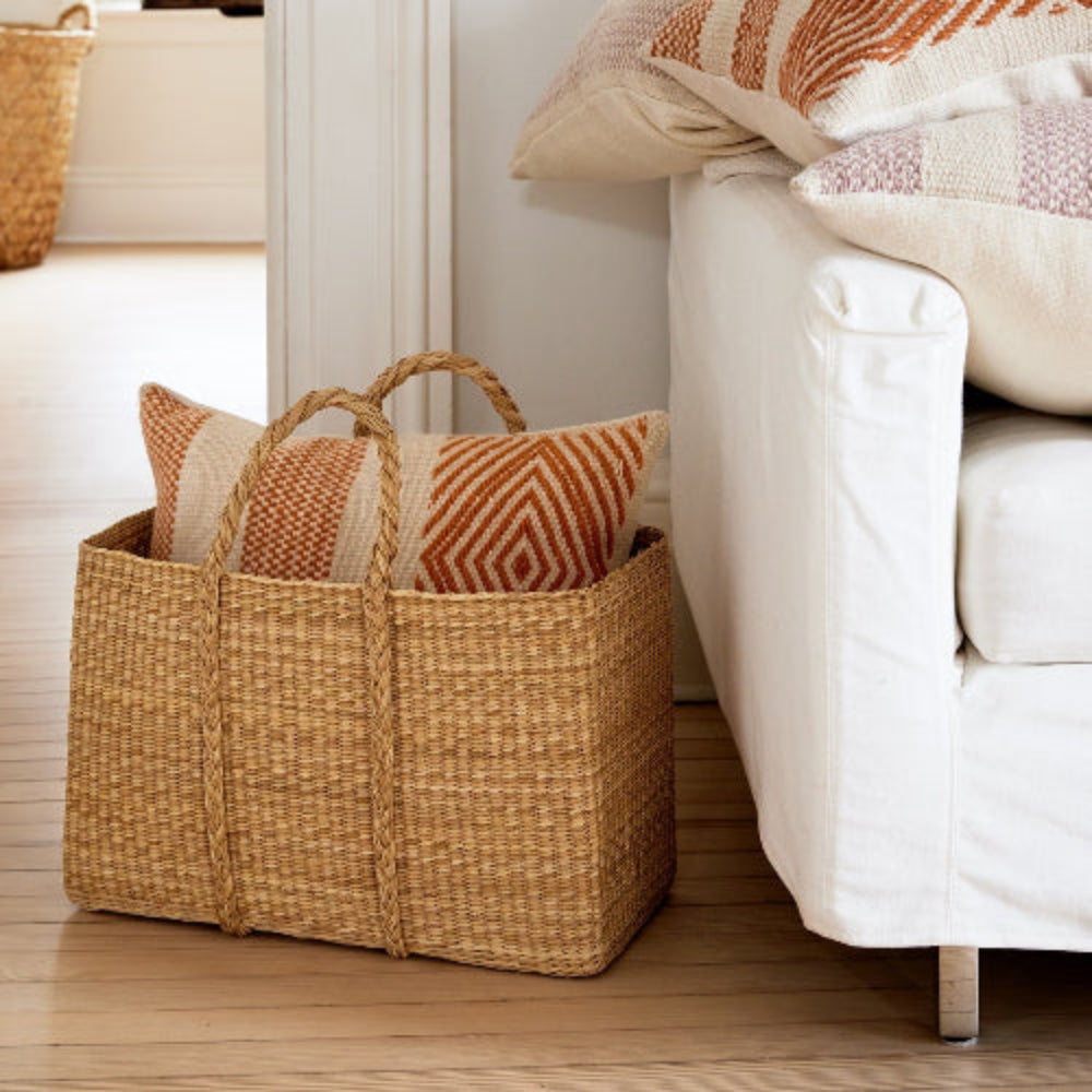 Wicker basket with decorative pillows on a white sofa in a bright room.
