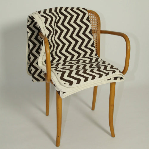Wooden chair with a zigzag patterned blanket on a plain background