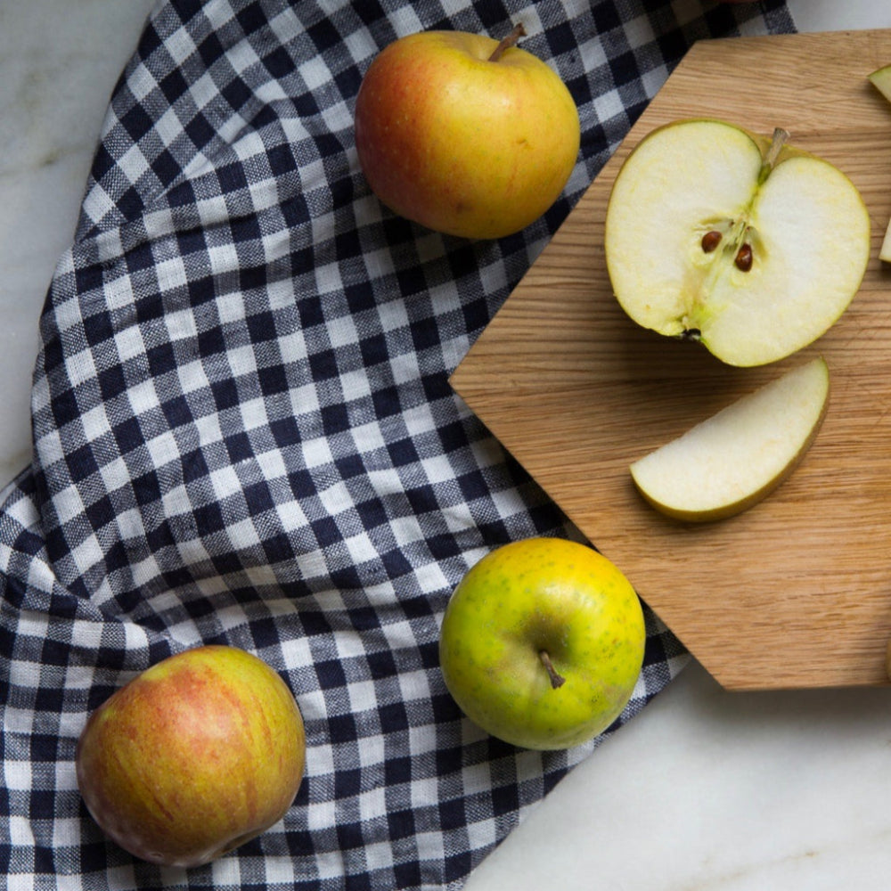 Apples on a checkered kitchen towel with a wooden cutting board