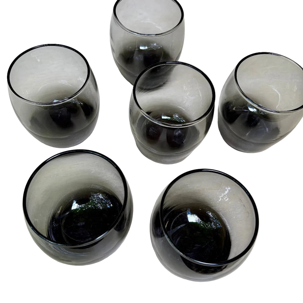 Five dark gray smoky glass tumblers arranged on a light beige surface.