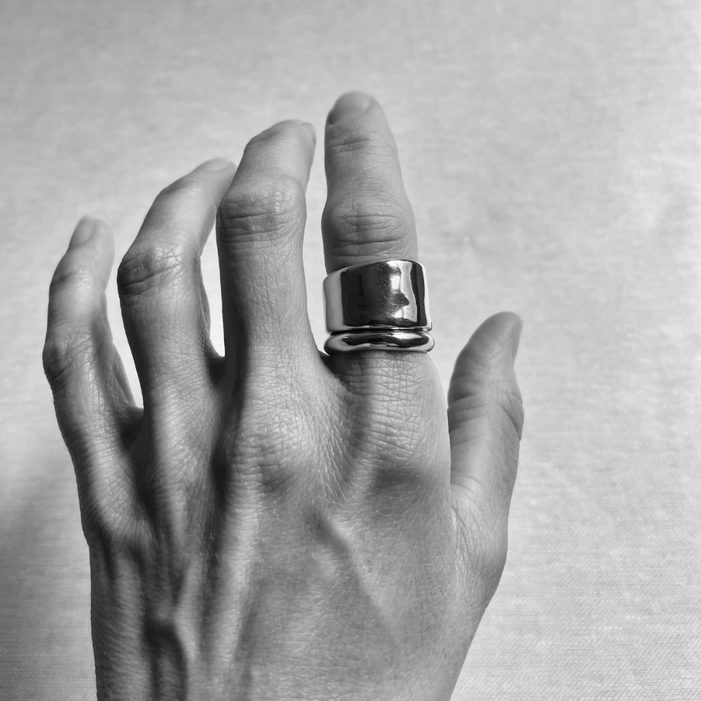 Hand wearing a large silver ring on a plain background