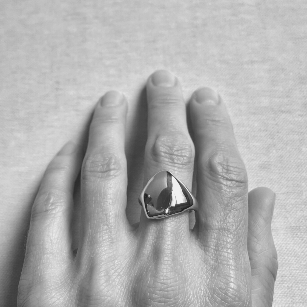 Hand wearing a large, faceted silver ring on a neutral background
