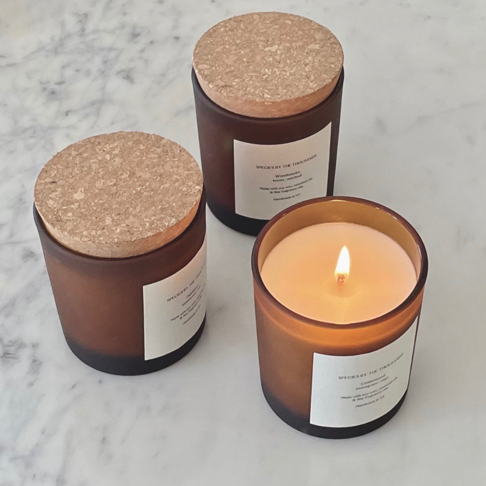 Three candles with cork lids on a marble surface, one of which is lit.