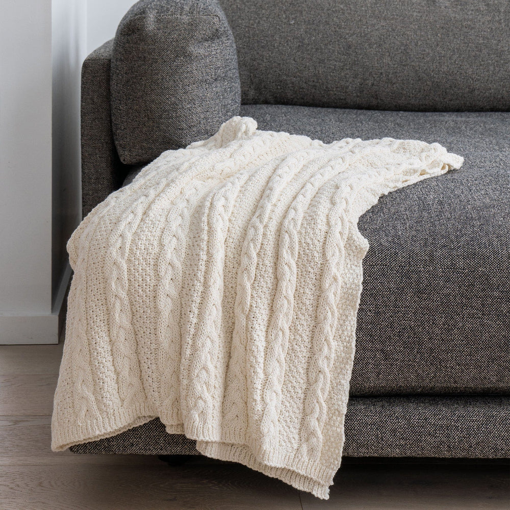 Beige cable knit blanket draped over a gray sofa