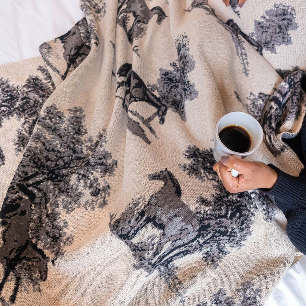 Person holding a cup of coffee over a patterned blanket with horse designs.
