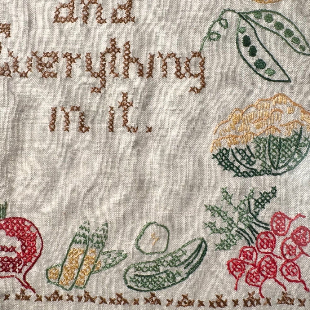 Embroidered fabric with vegetables and text on a beige background