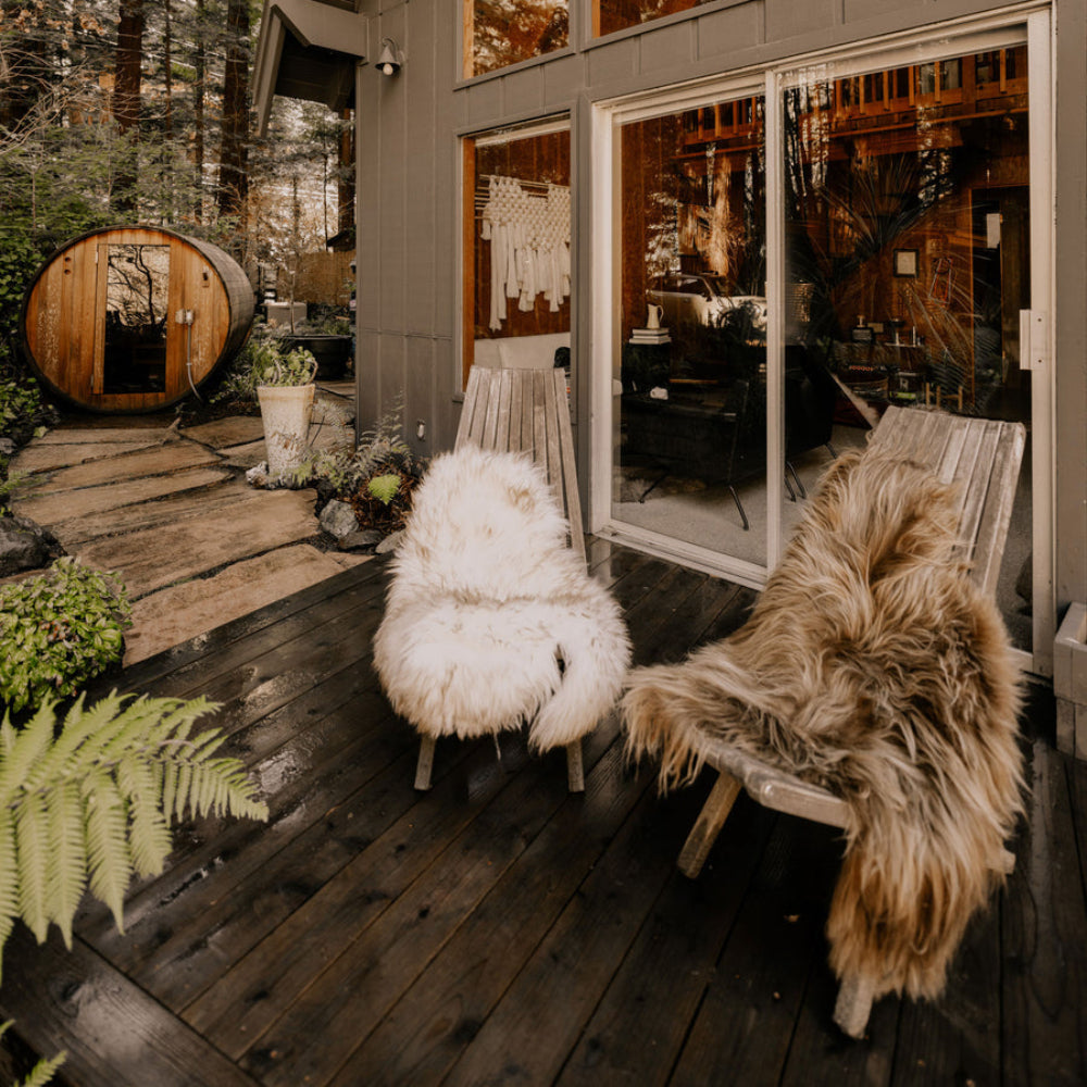Wooden cabin with large windows in a forest setting with sheepskin throws on chairs