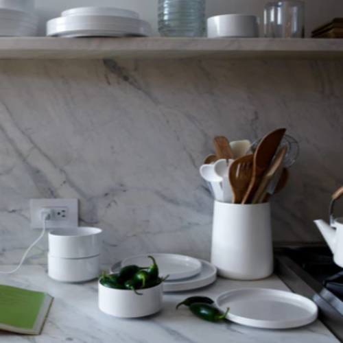 Kitchen counter with utensils, plates, and a book on a marble backsplash.
