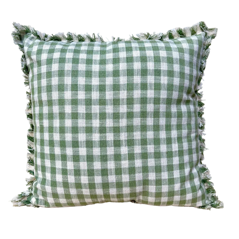A square throw pillow with a green and white gingham check pattern and fringed edges, resting on a light wood surface against a white background.