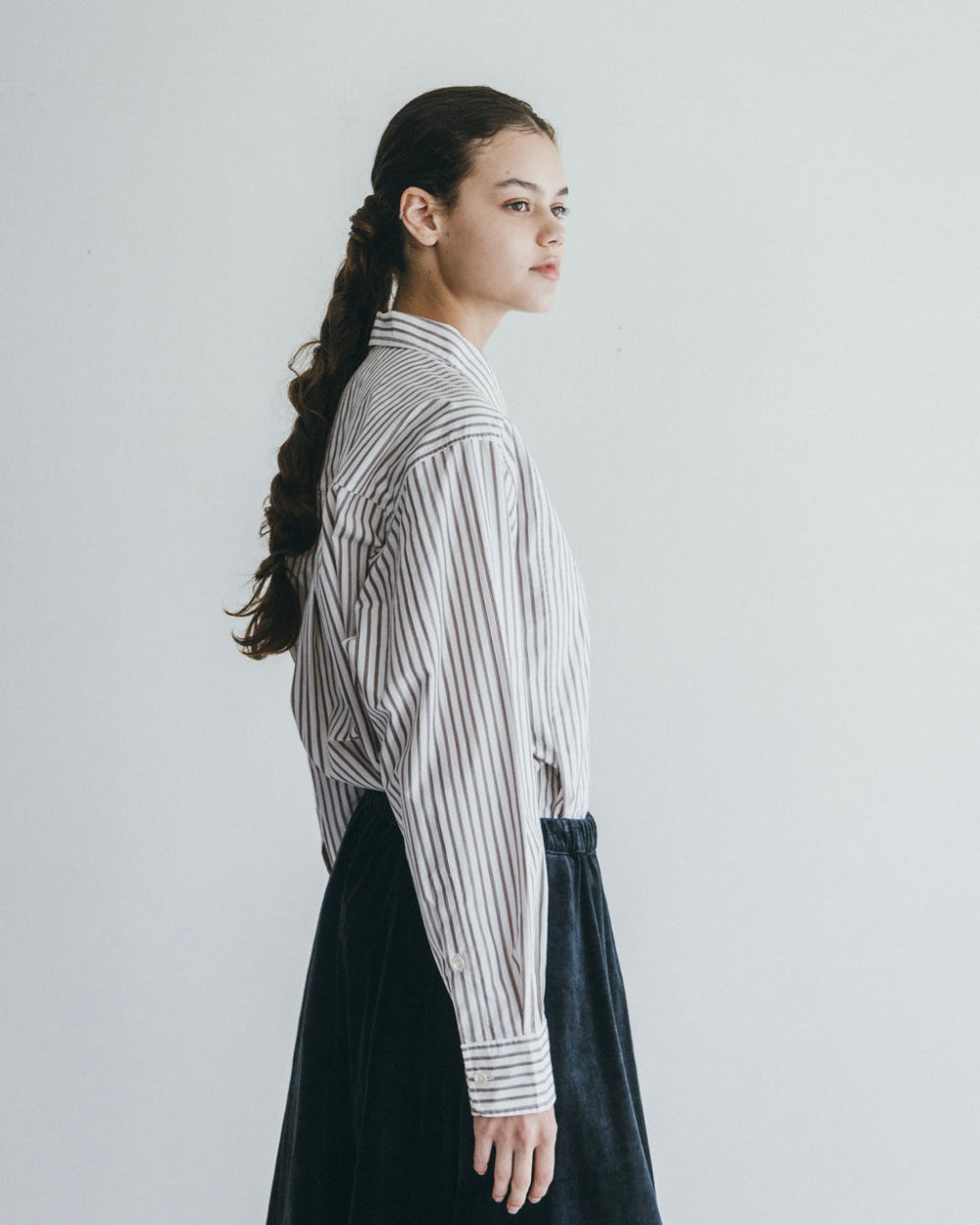 Person wearing a striped shirt and dark pants against a plain background