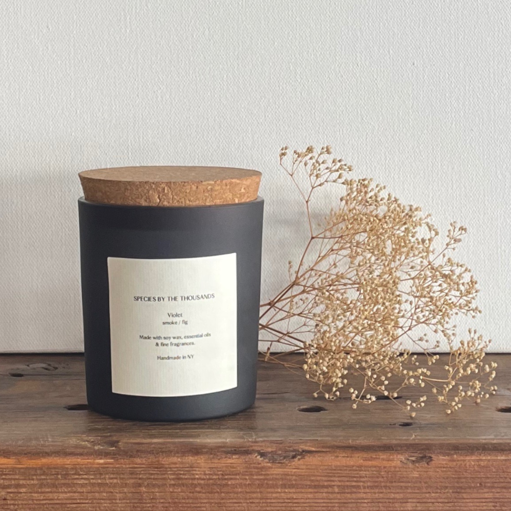 Black candle with wooden lid on a wooden surface with dried flowers