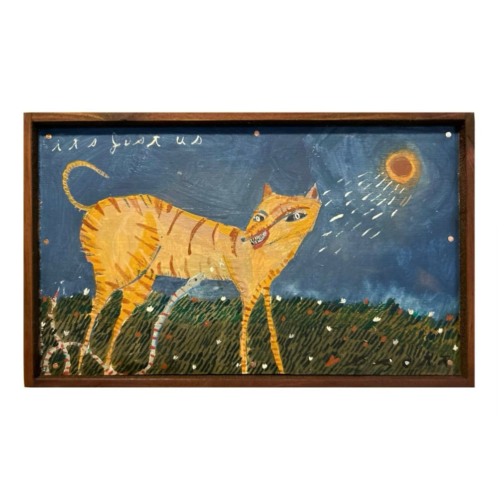 A framed folk art painting featuring a yellow-orange cat with black stripes standing in a grassy field at night under a dark blue sky with a glowing sun. The artwork is enclosed in a dark brown wooden frame and shown against a plain white background.