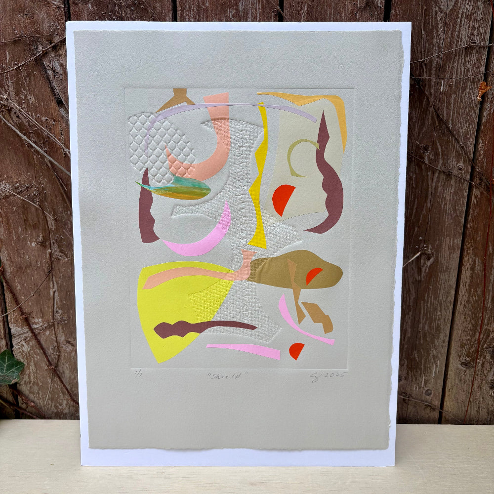 Abstract artwork with colorful shapes on a gray background, displayed against a wooden wall.