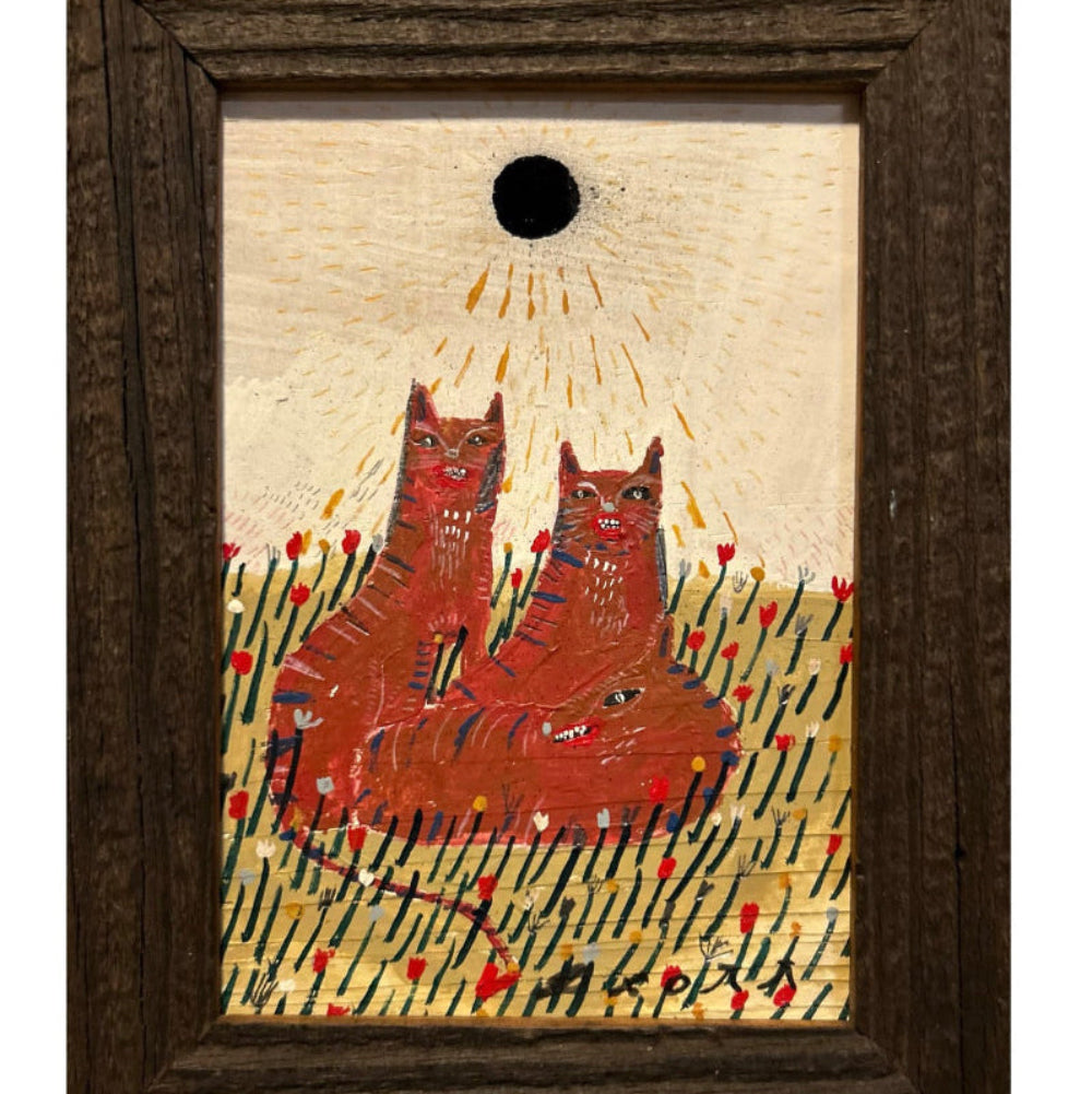 A framed folk art print depicting two red cats in a grassy field under a black sun on a beige background, enclosed in a dark brown wooden frame.
