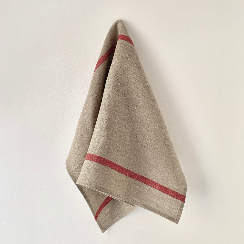 A beige kitchen towel with red stripes, hanging on a wall.